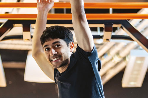 Man smiling while hanging from an orange bar in a gym.