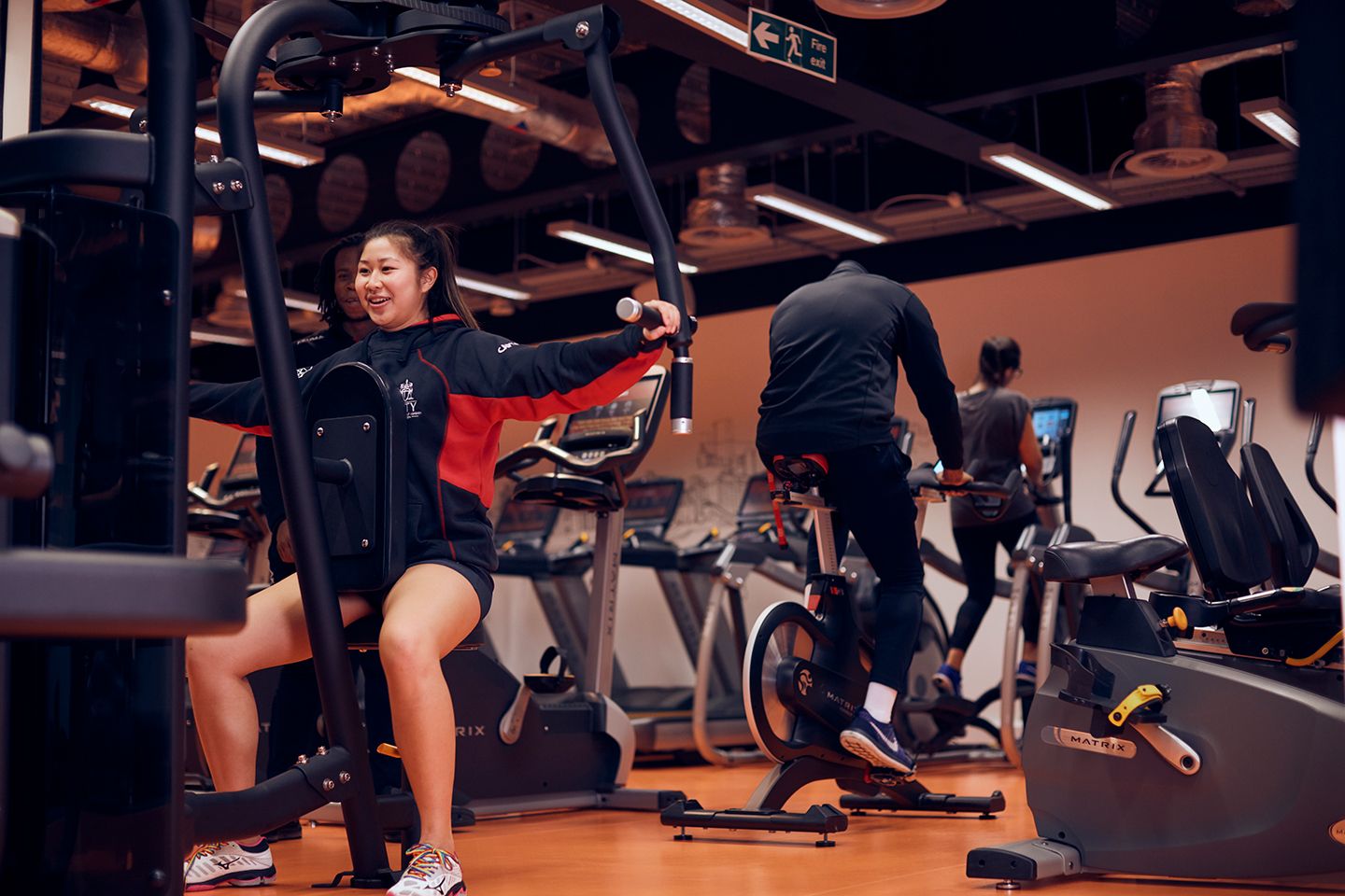 Student using a chest press machine with two others exercising nearby.