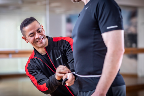 Personal trainer Itamar Peixoto measuring a man's waist with a tape in the gym