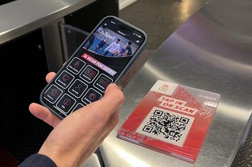 Person holding a phone with the CitySport app, scanning to open an entry gate.