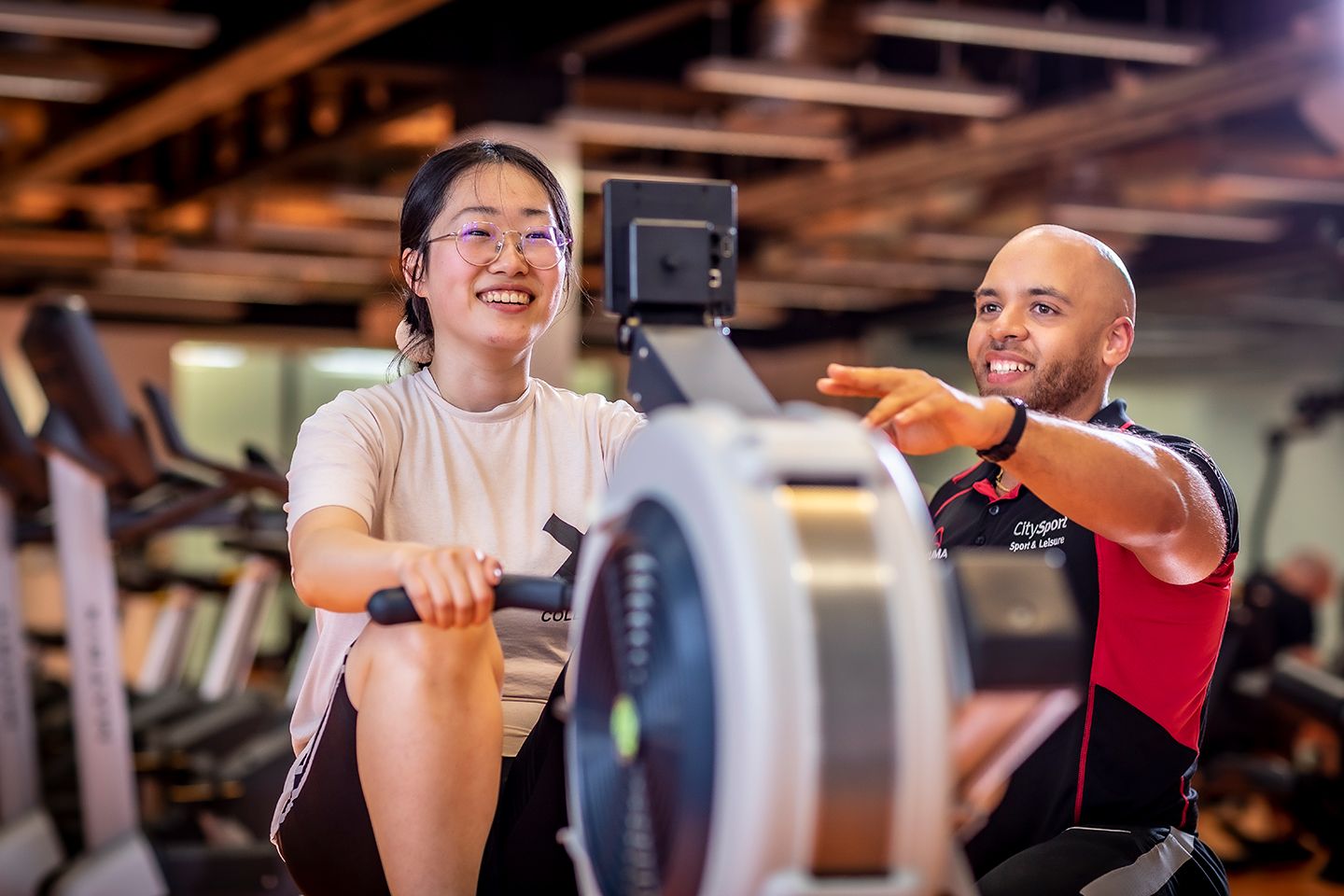 Personal trainer guiding a student on a rowing machine in a gym.