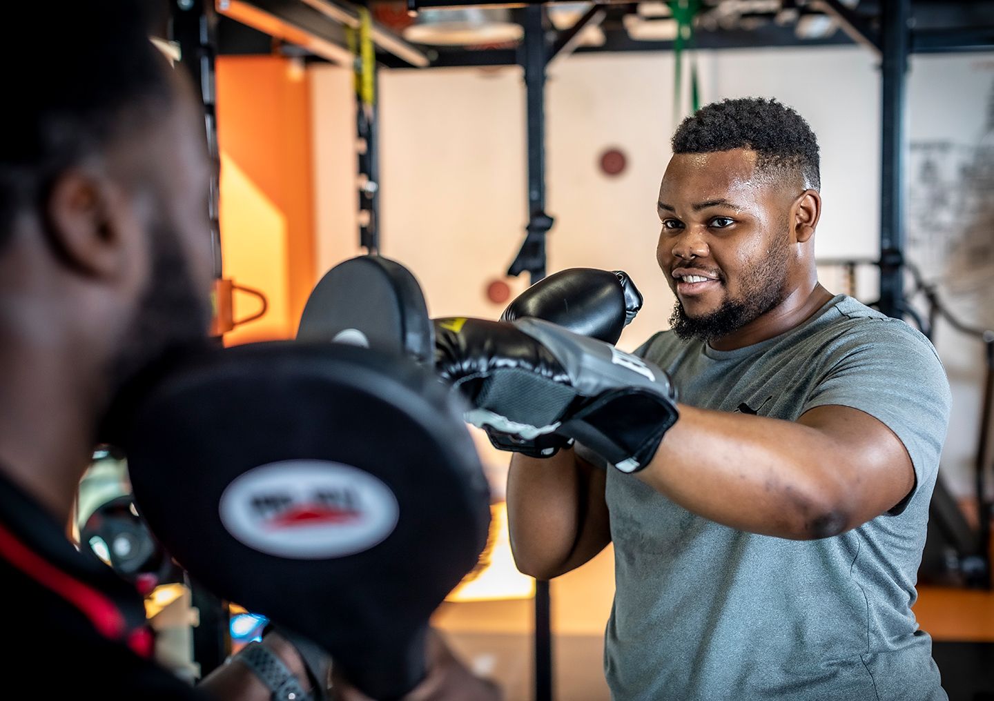 Man boxing with a trainer holding pads in the gym.