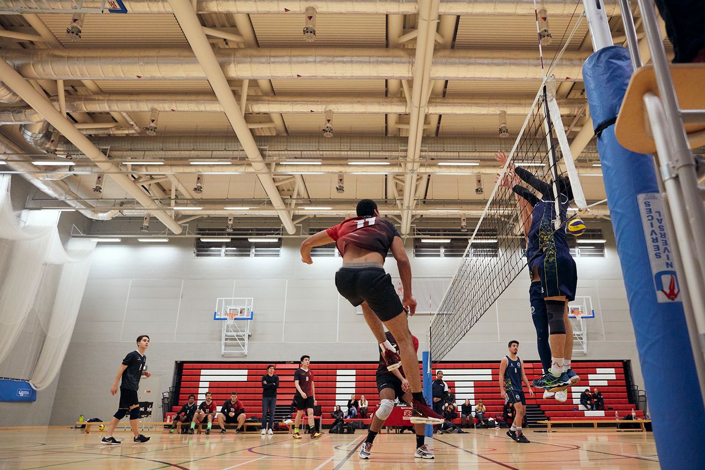 Indoor volleyball match with a player striking the ball as opponents attempt to block.