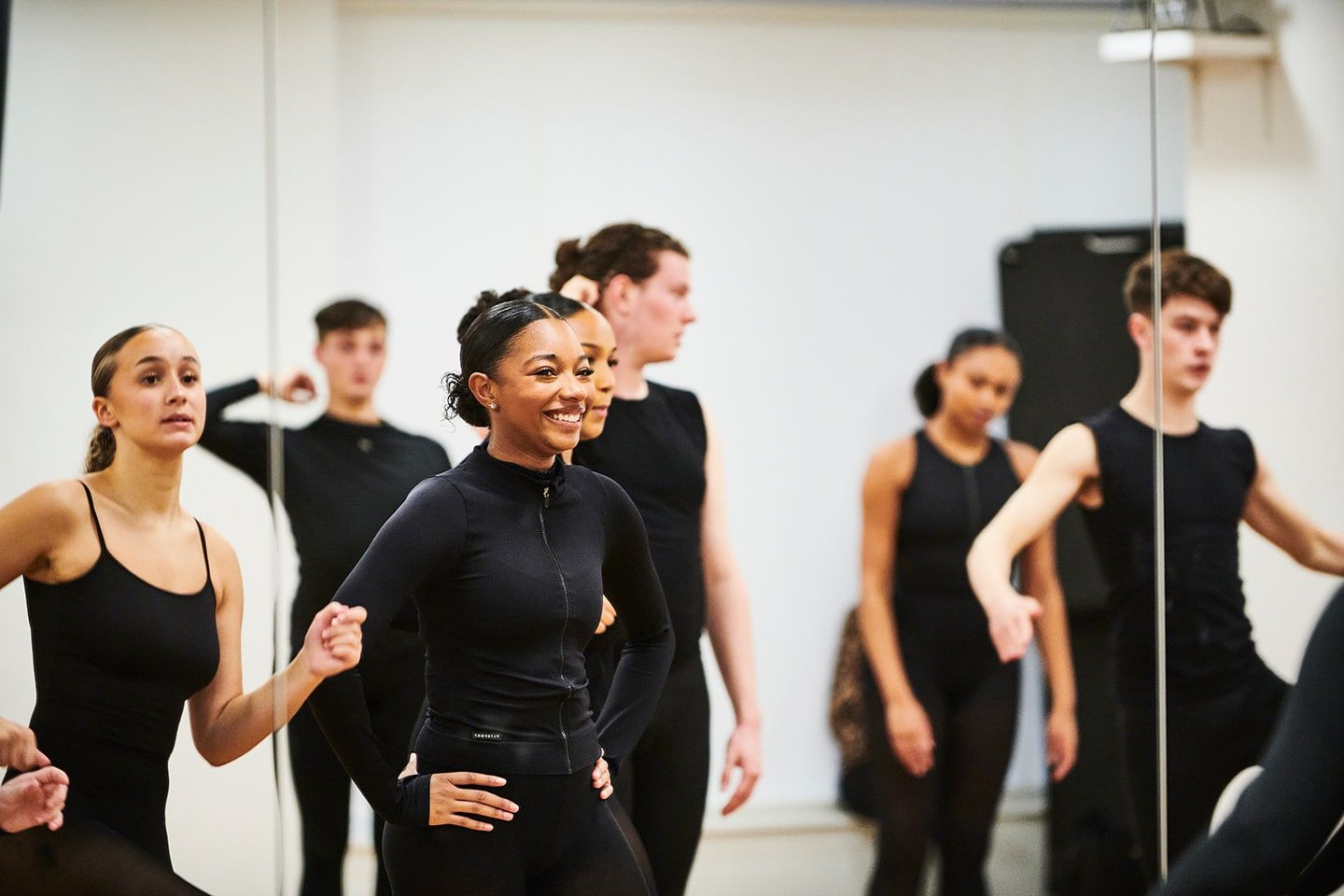 Group of young dancers in black attire practicing in a studio.
