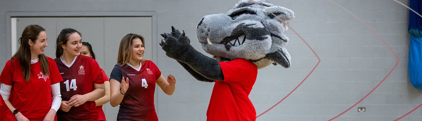 CitySport wolf mascot cheering with three women sports team players in the sports hall.