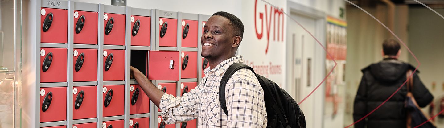 Student smiling while using lockers in the university gym changing area.